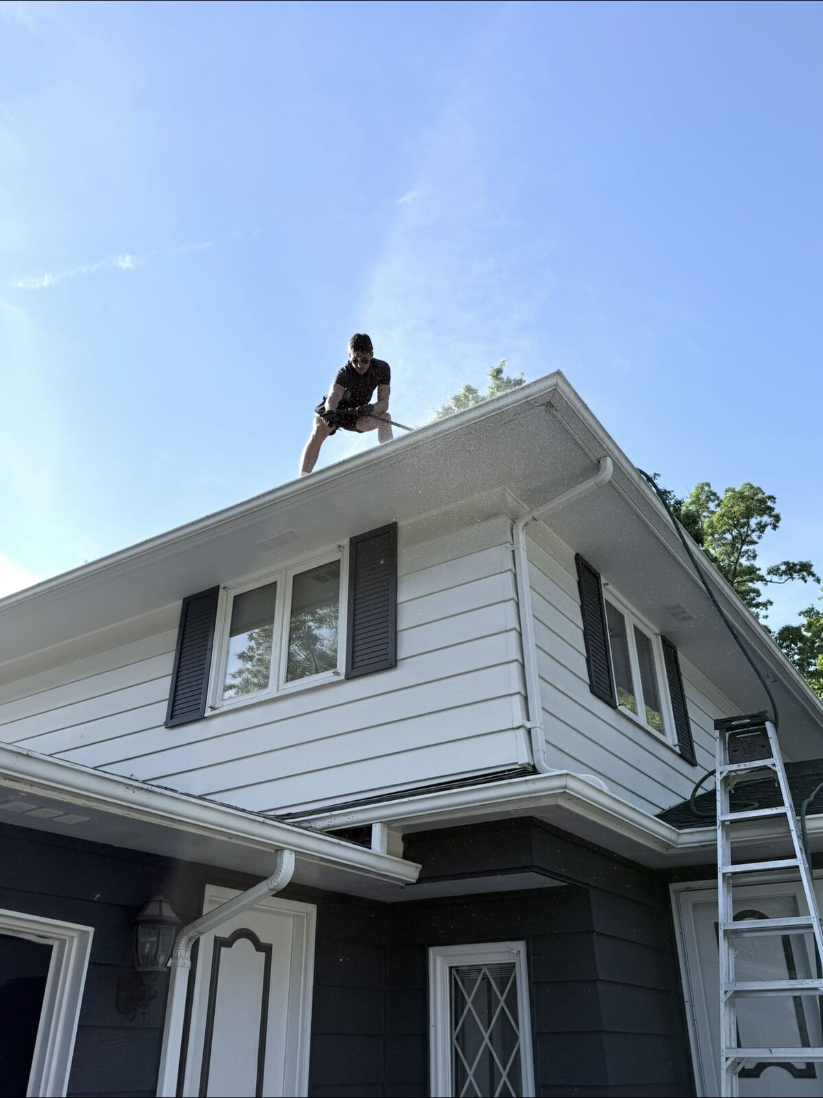 Crew member power washing a gutter from a second-story roofline