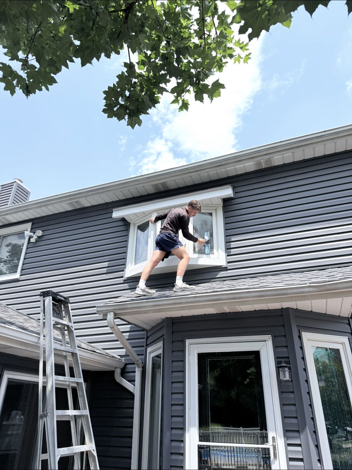 Crew member cleaning a dormer window from the roofline